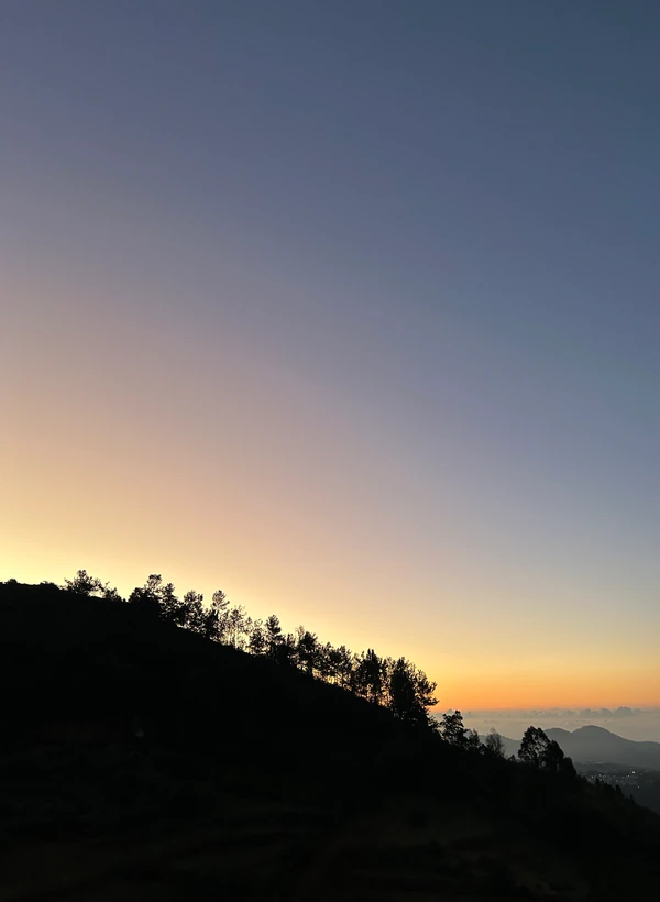 A sunset behind a tree-lined hillside, photographed by Sumit